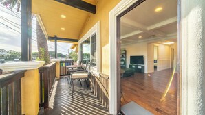 Varanda coberta com piso de madeira, área de estar com cadeiras e vista para o interior de uma casa.
