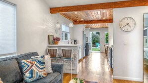 A modern kitchen with a central island, wooden ceiling beams, and a dining area with bar stools. - Del Monte Beach Cottage Sleeps 4 with Private Yard (Seaside)