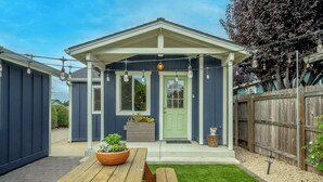A blue house with a green door, a wooden fence, and a picnic table with a potted plant. - Del Monte Beach Cottage Sleeps 4 with Private Yard (Seaside)