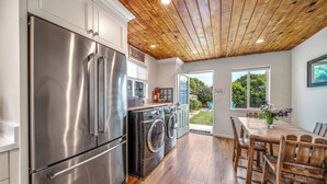 A kitchen with stainless steel appliances, wooden flooring, and a dining area with wooden chairs. - Del Monte Beach Cottage Sleeps 4 with Private Yard (Seaside)