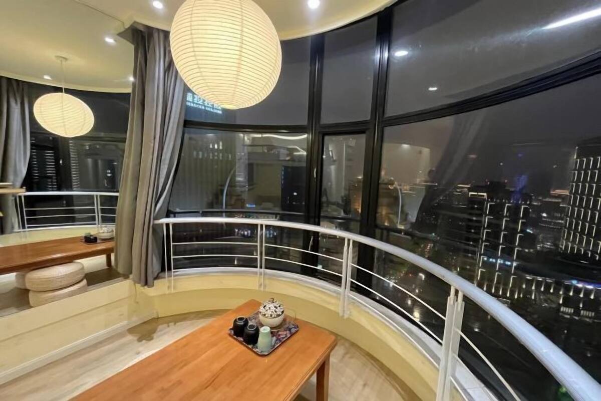 A modern hotel room with a balcony, large windows, and a city view.