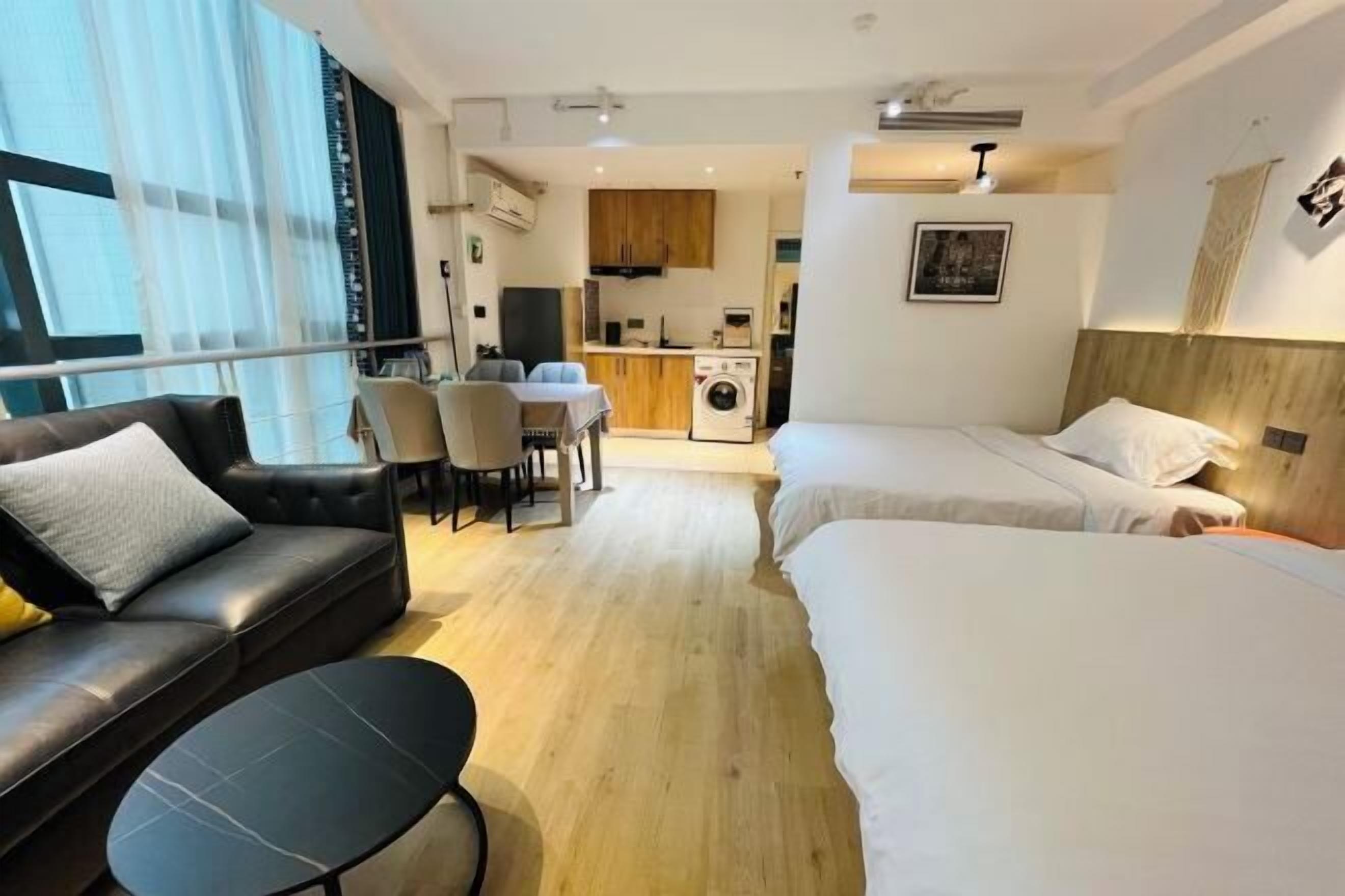 A modern hotel room with a sofa, a small table, a bed, and a kitchenette in the background.