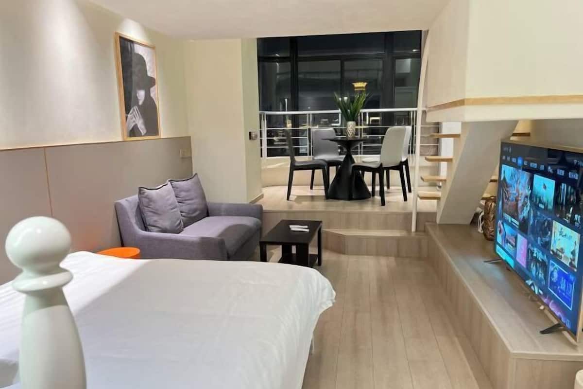 A hotel room with a bed, a sofa, a TV, a balcony with a table and chairs, and a large window.