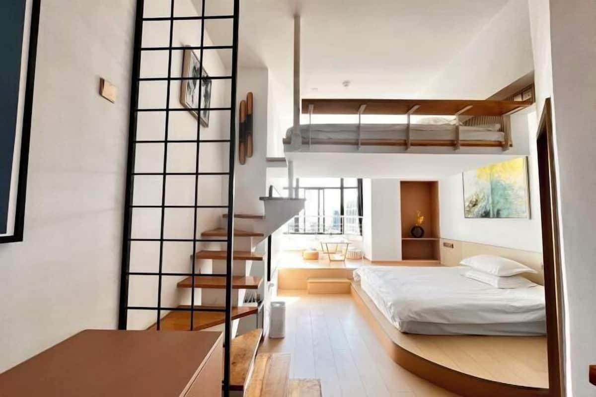 A modern loft bedroom with a loft bed, a staircase, and a view of the city.