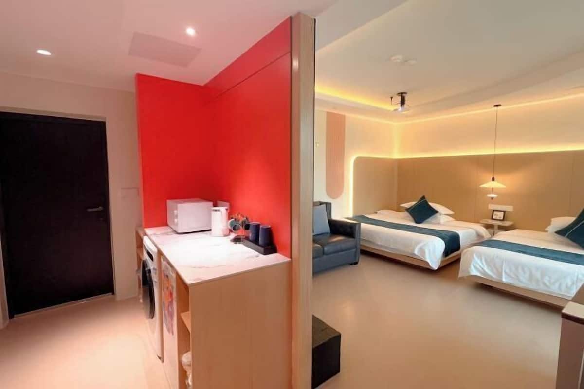 A hotel room with a red accent wall, two beds with white linens, a desk with a microwave, and a washing machine.
