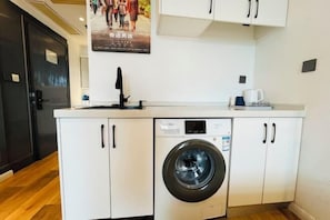 Une cuisine compacte dotée d’un lave-linge encastré, de meubles blancs et d’une machine à café.