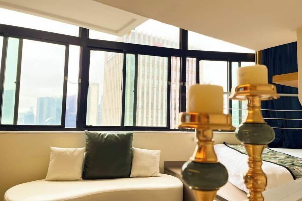 A hotel room with a large window, a sofa, and a bed with a decorative lamp.