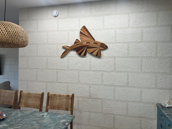 Un coin repas agrémenté d’un mur à texture, d’une décoration représentant un avion en bois, de chaises en osier et d’une table dont le plateau ressemble à du marbre.