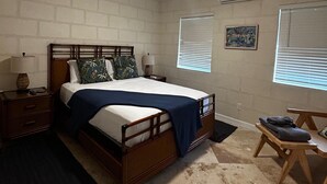 A bedroom with a wooden bed, a nightstand, a small table, and a ceiling fan. - Villa By The Bay
Luxury 3 bedroom all ensuite, private pool, pickleball court (Bridgetown)