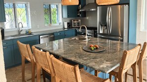 A modern kitchen with teal cabinets, a large island with chairs, a stainless steel refrigerator, and a hanging light fixture. - Villa By The Bay
Luxury 3 bedroom all ensuite, private pool, pickleball court (Bridgetown)