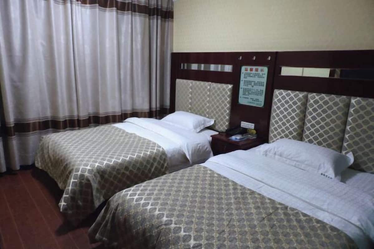 Quarto de hotel com duas camas, uma cabeceira de madeira, uma mesa de cabeceira e uma cortina.