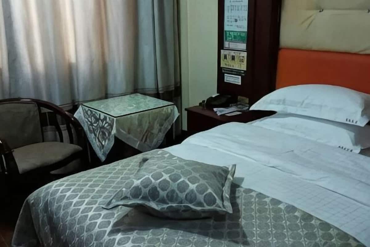 Quarto de hotel com uma cama, uma pequena mesa com toalha e uma cadeira. Há também um mural na parede.