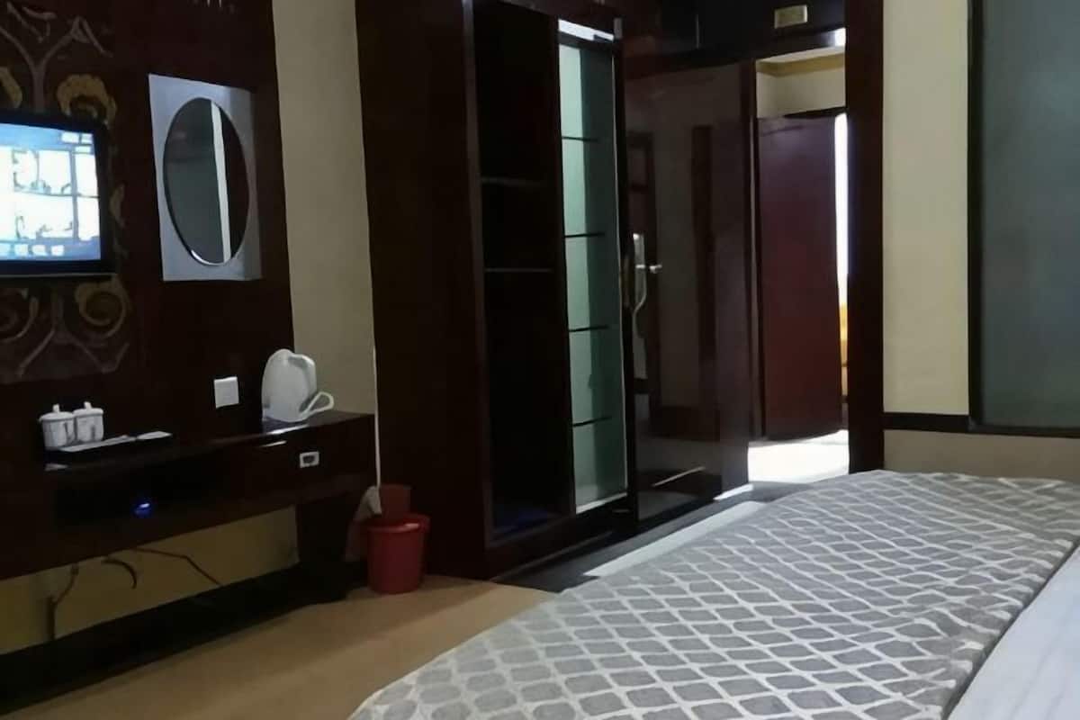 Quarto de hotel com cama, televisão, espelho, guarda-roupa e um cesto de lixo vermelho.