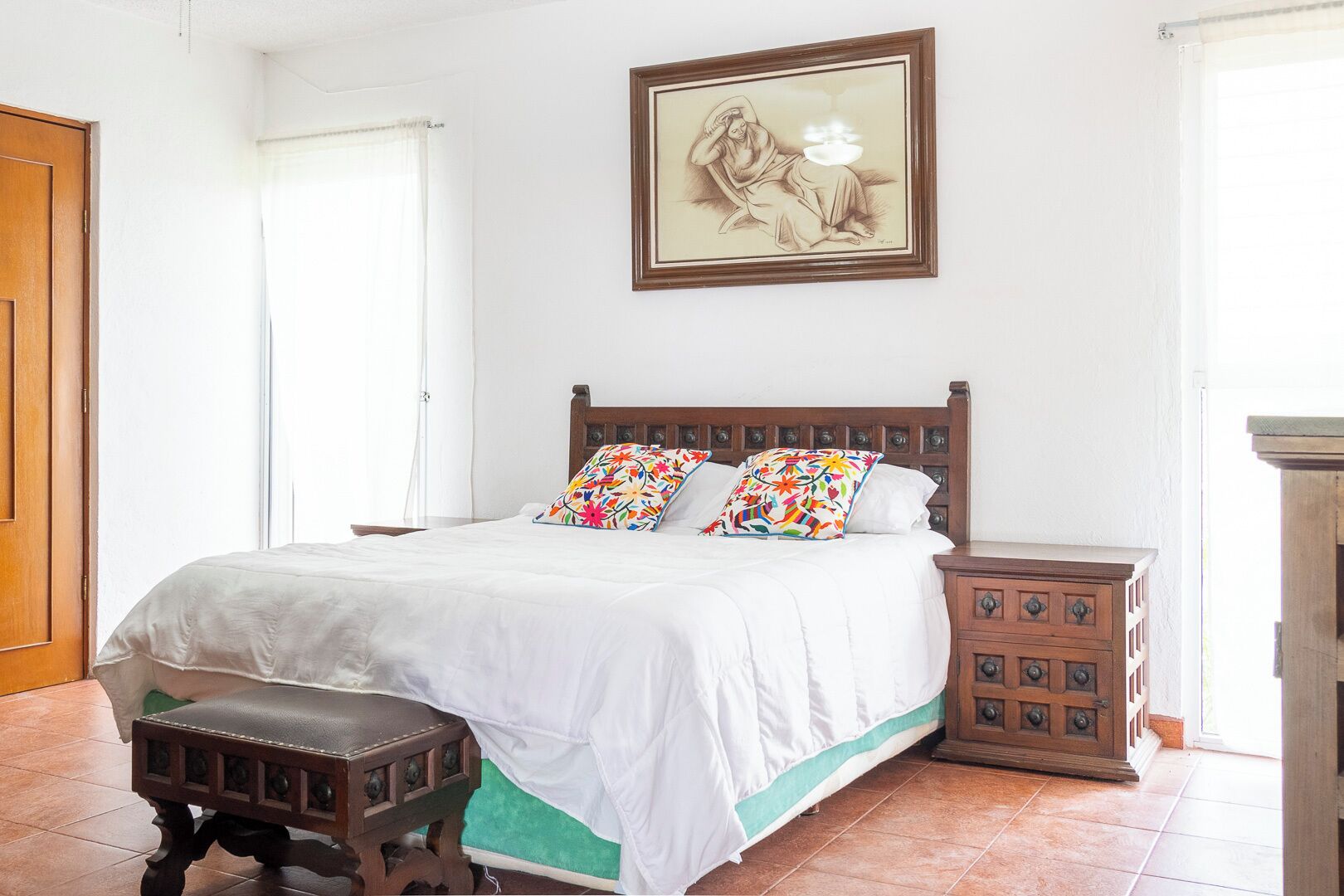 Ein Schlafzimmer mit einem hölzernen Bett, bunten Kissen, einem Nachttisch und einem gerahmten Kunstwerk an der Wand.