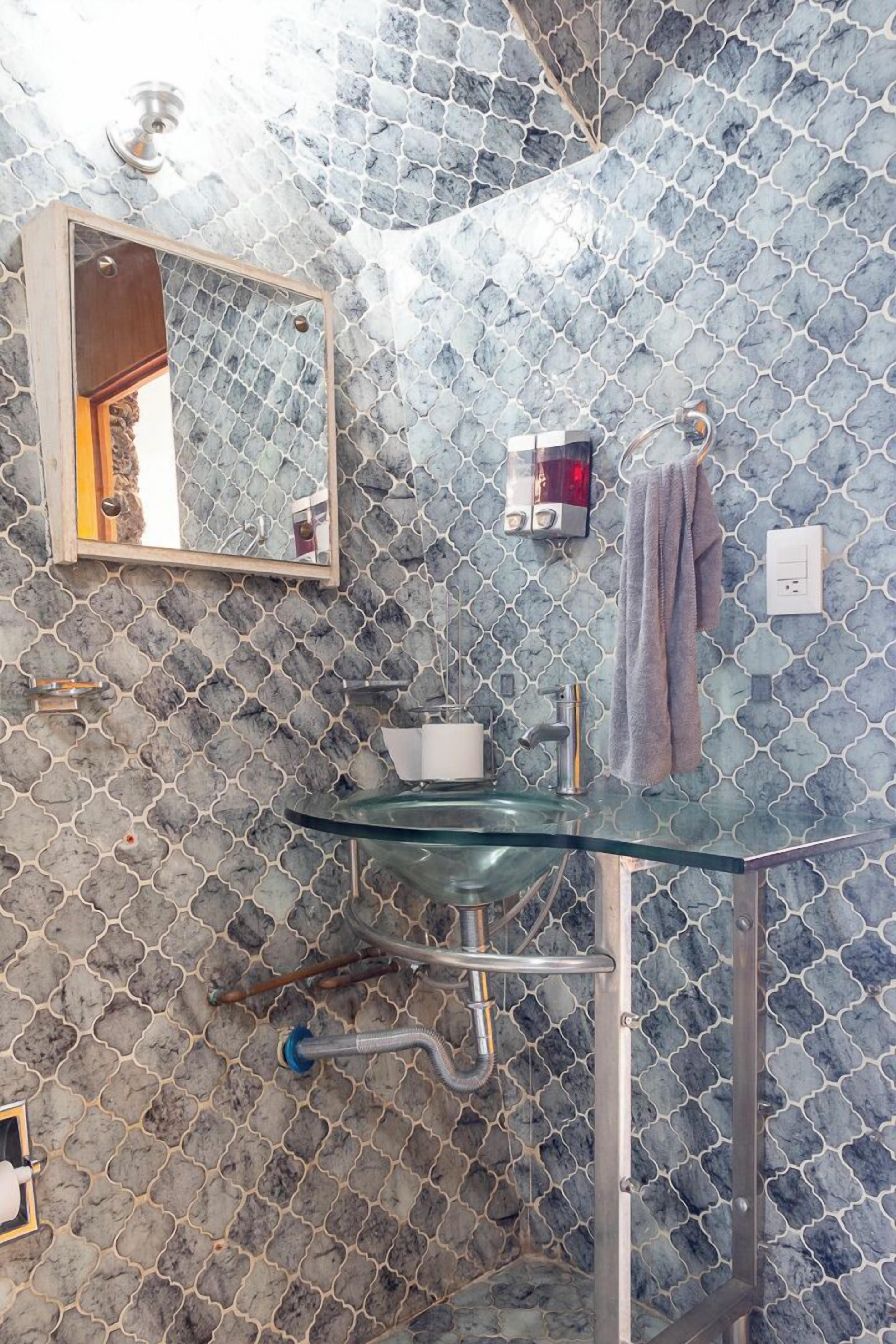 A bathroom with a glass sink, a mirror, and a towel rack.