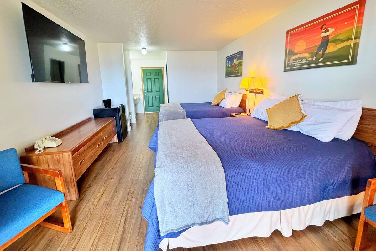 Una habitación de hotel con dos camas, un escritorio, una silla, un televisor y una puerta.