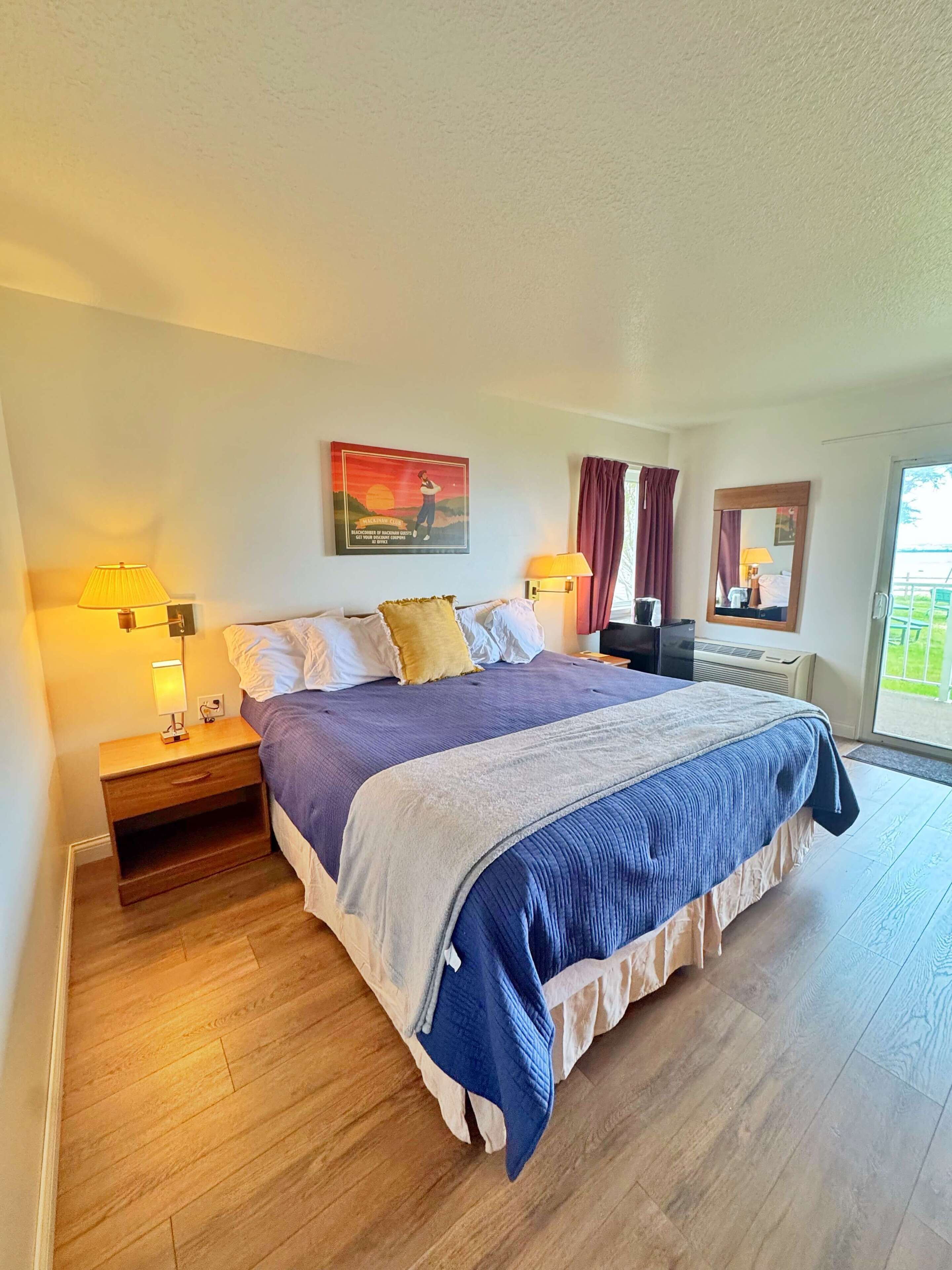 A hotel room with a bed, nightstands, a lamp, a painting, a mirror, and a window with curtains.