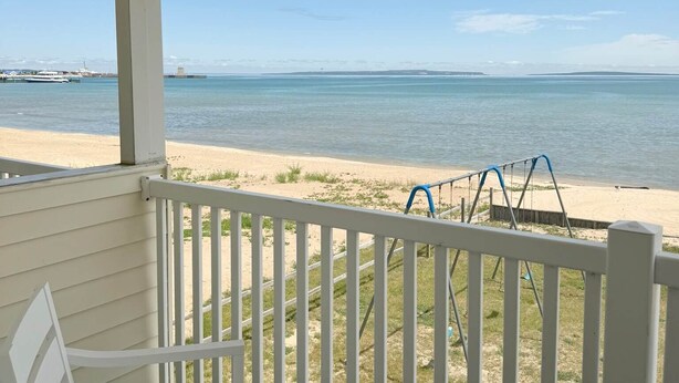 Un balcon abrité avec une chaise blanche, une balançoire et une vue sur la plage et l’océan.