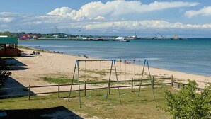 Une plage avec des balançoires, un rivage sablonneux et une vue sur un pont et un navire au loin.