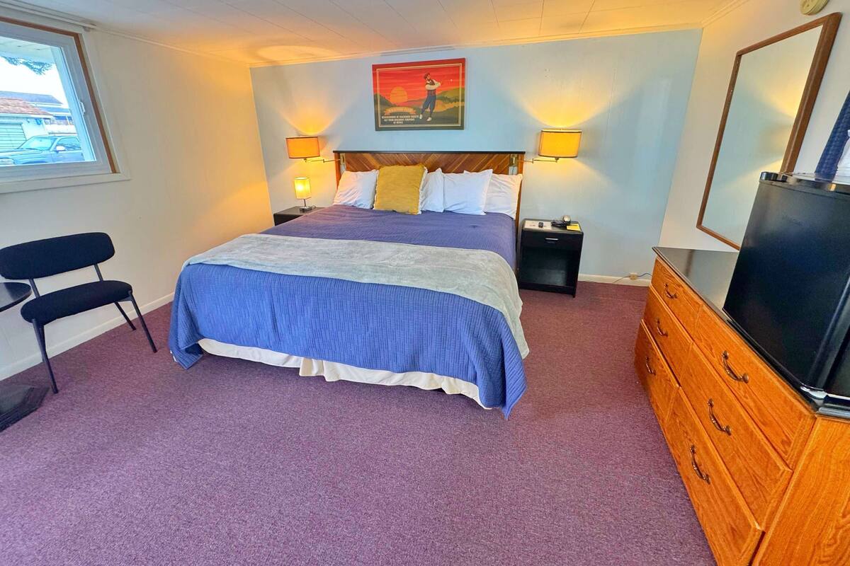 Un dormitorio con una cama, dos mesitas de noche, un tocador, una silla y una ventana.