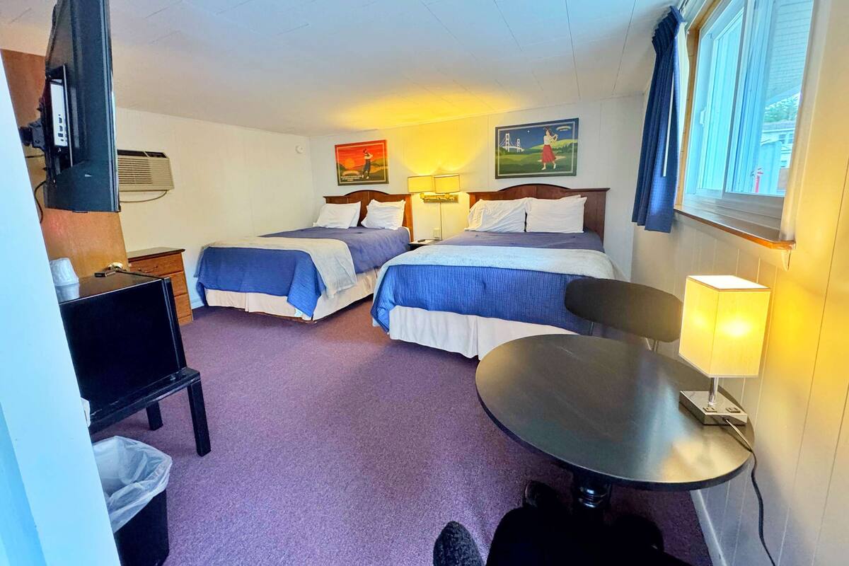Habitación de hotel con dos camas, un escritorio, una silla, una lámpara y una ventana.