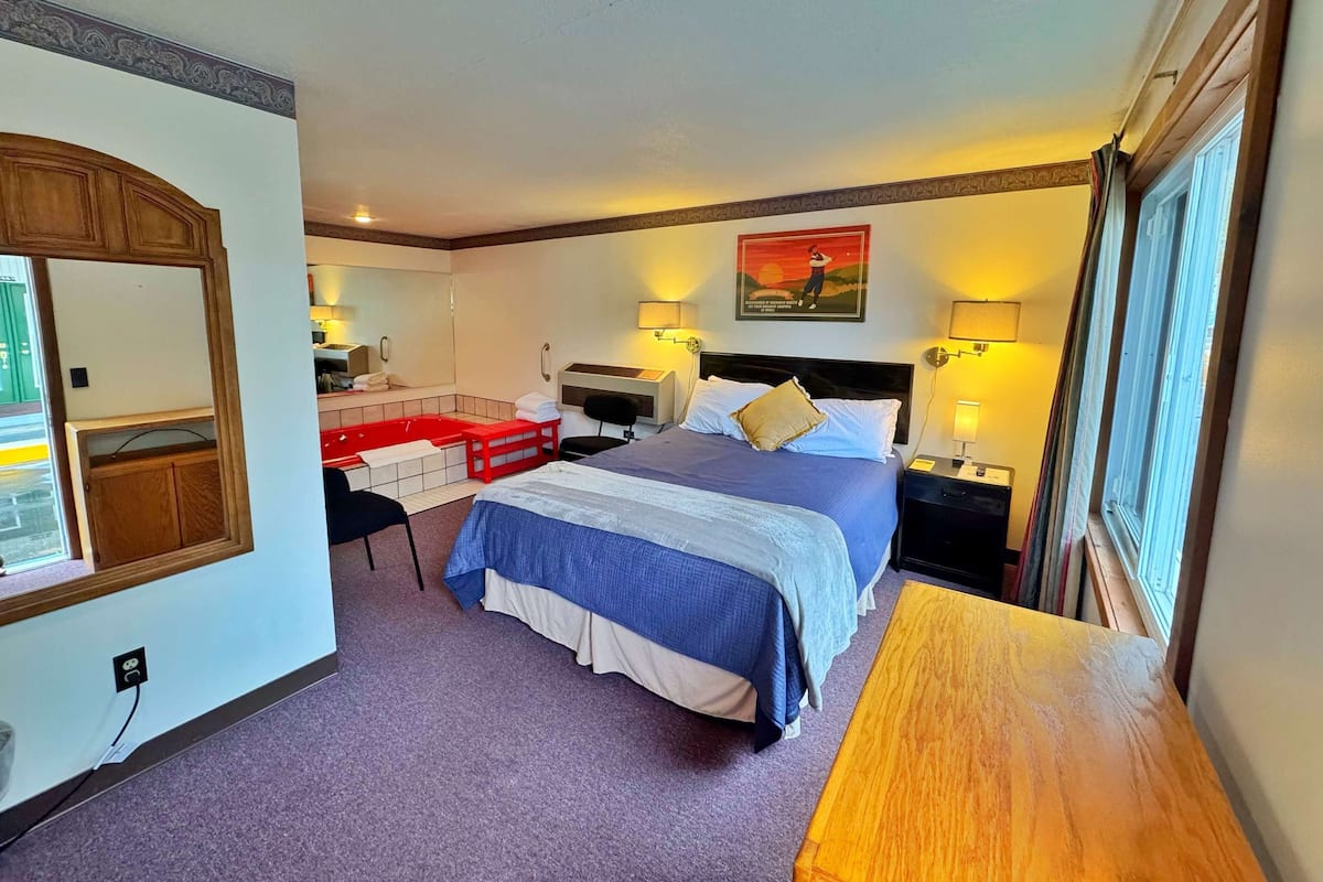 Habitación de hotel con cama, mesitas de noche, escritorio, silla, bañera roja y ventana.