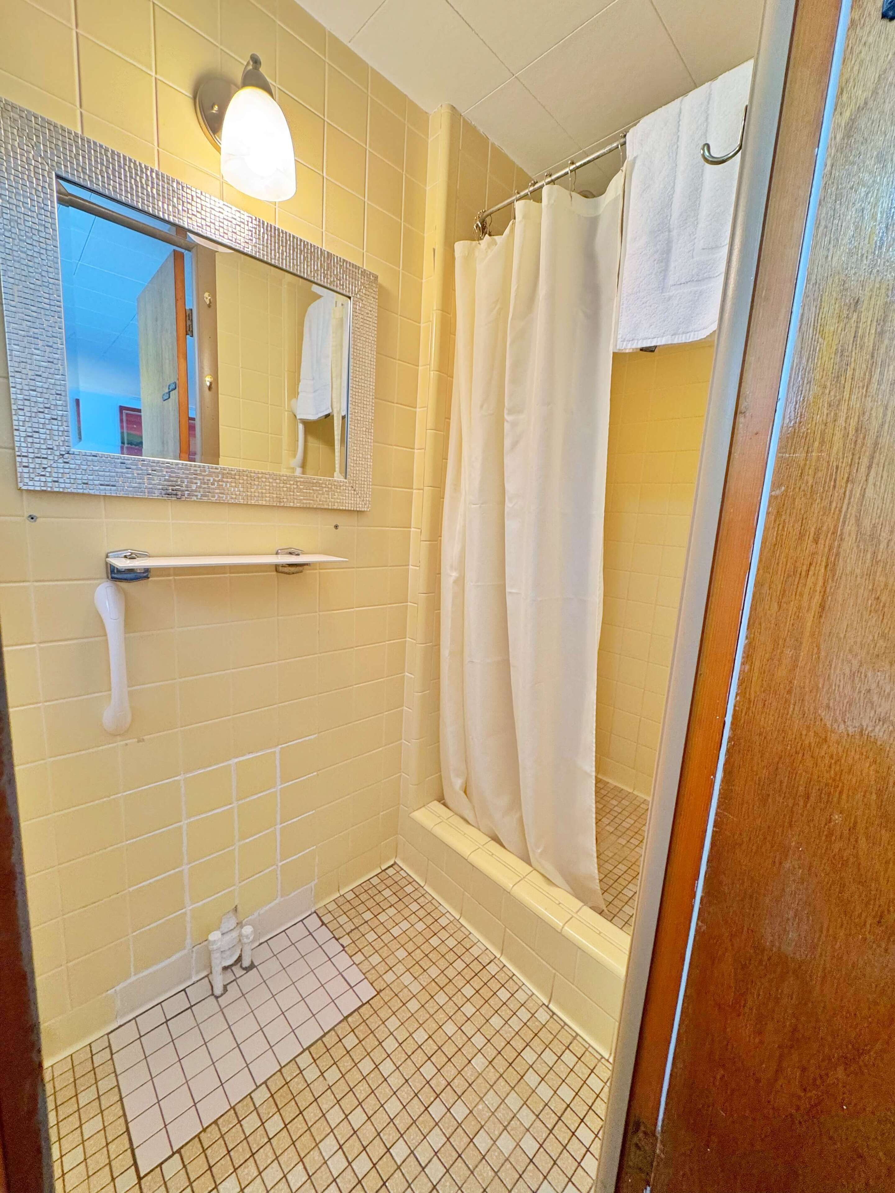 A small bathroom with yellow tiles, a white sink, a mirror with a mosaic frame, a shower curtain, and a towel hanging on the wall.