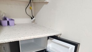Un petit réfrigérateur compact avec un intérieur blanc, un compartiment congélateur transparent et un petit bac de rangement violet sur l’étagère supérieure.