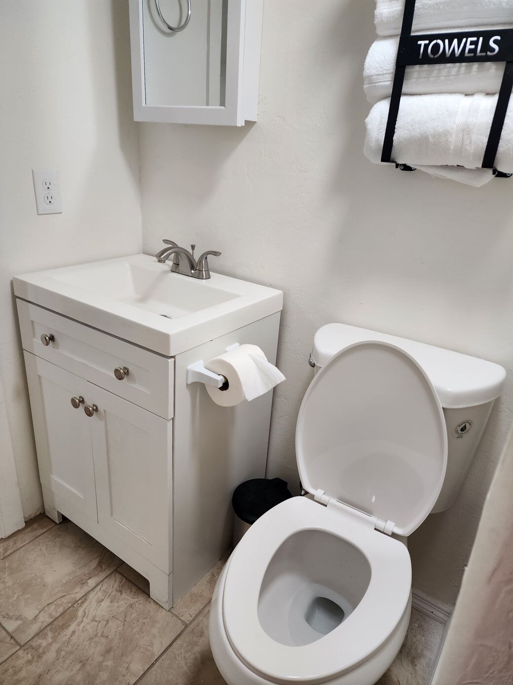 A bathroom with a white sink, toilet, and cabinet. There is a towel rack with towels above the toilet.
