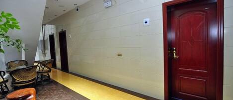 Un couloir d’hôtel avec une porte en bois, un comptoir de réception et un espace détente avec des chaises.
