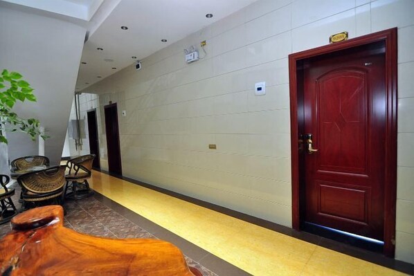 A hallway with a red door, a plant, and wicker furniture. - Luoping Star River Express Hotel (Luoping)