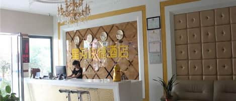 A hotel reception area with a reception desk, a chandelier, a sofa, and a potted plant.