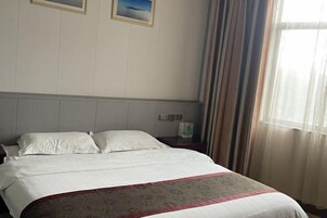 A hotel room with a bed, a nightstand, a telephone, and a window with curtains.