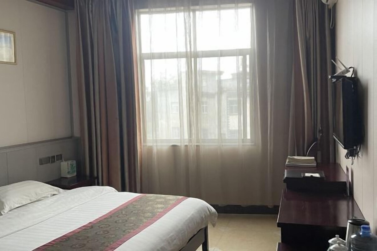 Una habitación de hotel con una cama, un escritorio con una silla, una ventana con cortinas y un televisor fijado a la pared.