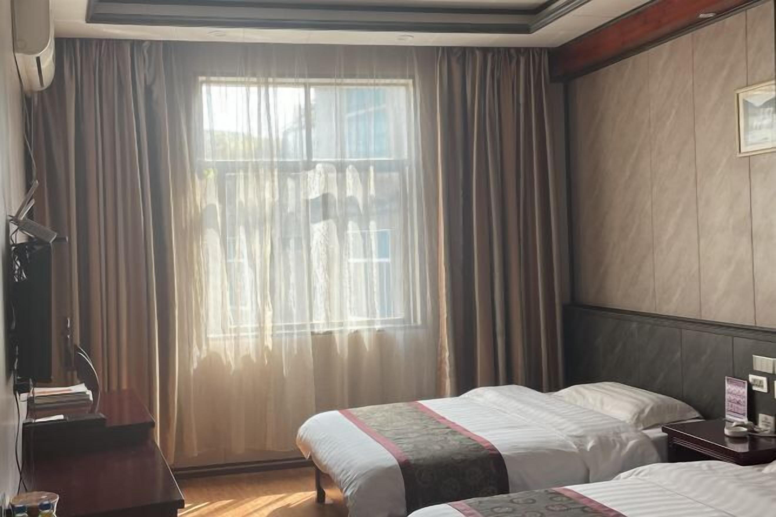 Habitación de hotel con dos camas, un escritorio con silla, televisión y ventana con cortinas.
