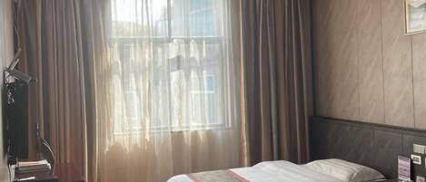 Habitación de hotel con dos camas, un escritorio con silla, televisión y ventana con cortinas.
