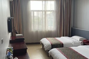 Una habitación de hotel con dos camas, un escritorio de madera, un teléfono y un ventanal con cortinas.