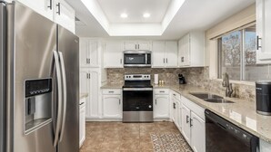 A modern kitchen with white cabinets, stainless steel appliances, a built-in oven, and a large window providing natural light.