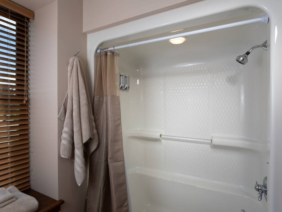 A bathroom with a bathtub, a towel rack with towels, and a window with blinds.