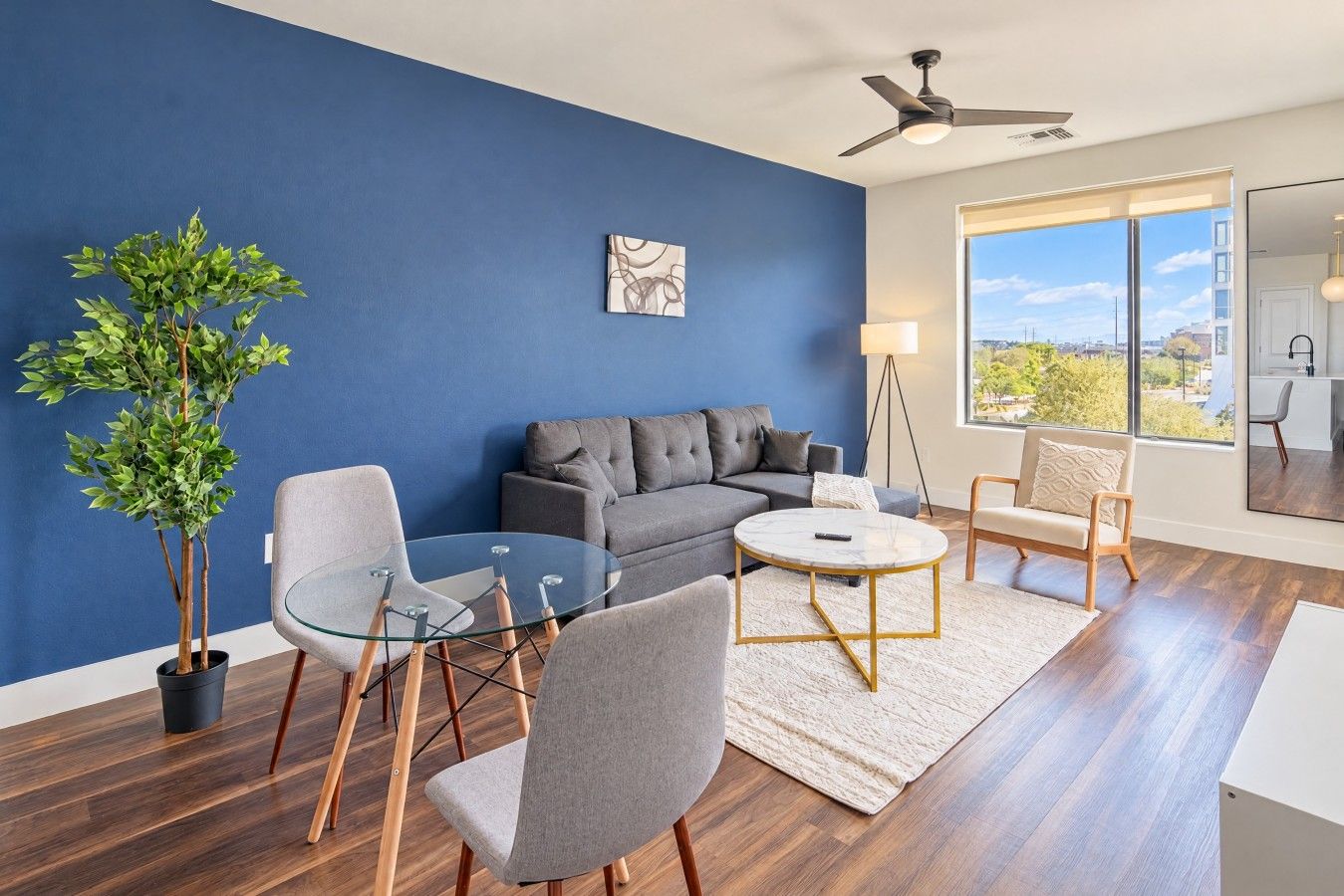 A modern living room with a blue accent wall, a grey sofa, a glass coffee table, and a potted plant.