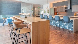 Un espace bar moderne avec des tabourets de bar en bois et des chaises bleues, une cuisine avec des meubles gris et un mur orné de motifs.
