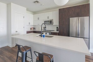 A modern kitchen with white cabinetry, a stainless steel refrigerator, and a central island with bar stools. - Heart of Tempe 1BD with Pool, Gym, Parking (Tempe)