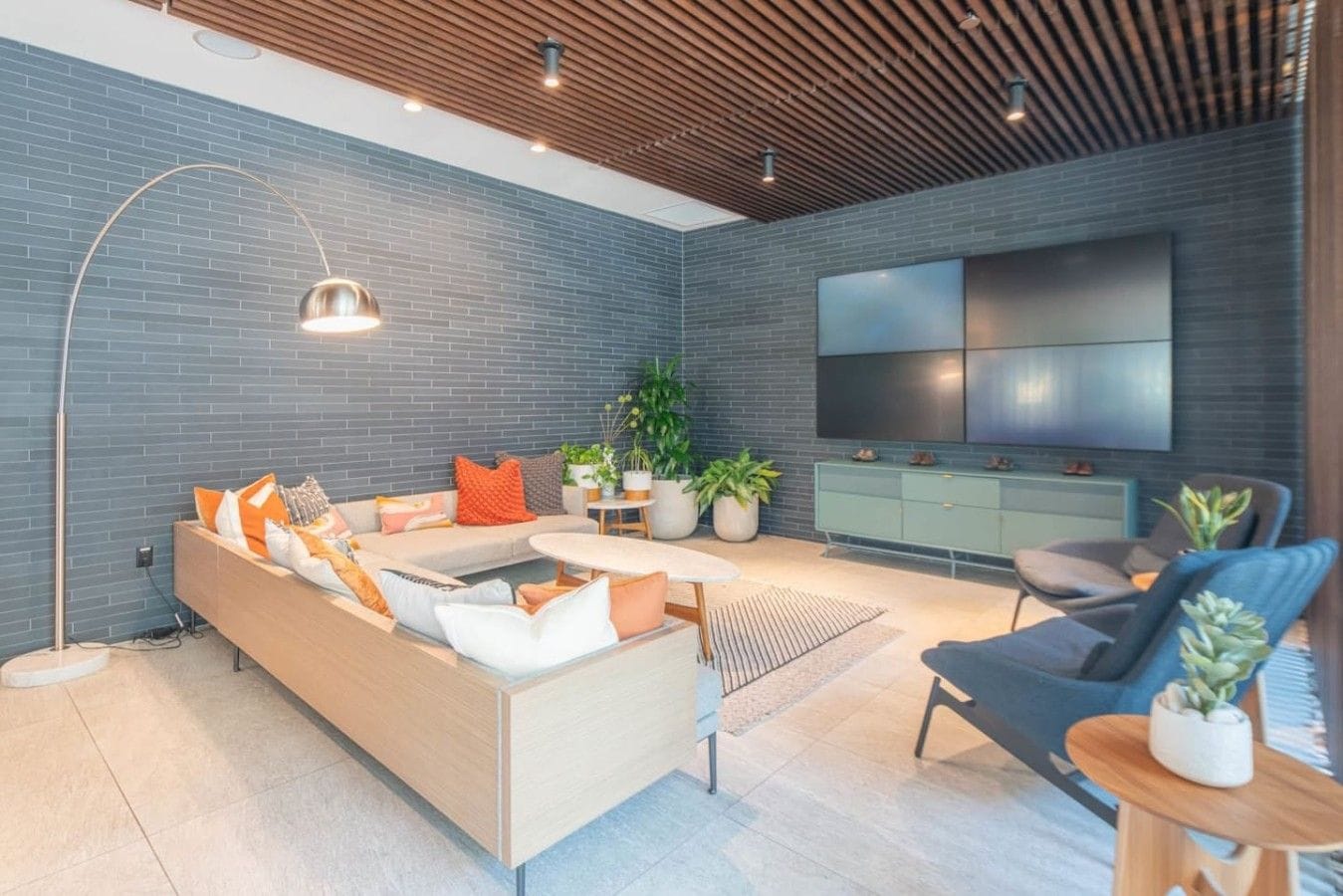 A modern living room with a sectional sofa, a coffee table, a TV mounted on the wall, and a potted plant.