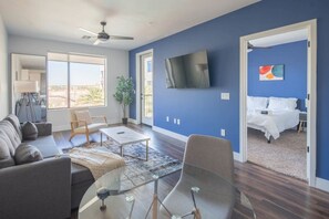 Una sala de estar moderna con sofá, mesa de centro y televisor. En la habitación contigua hay una cama con vistas.