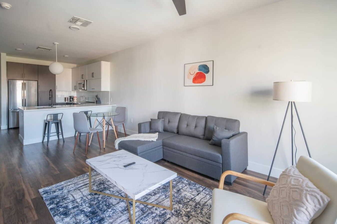 A modern living room with a grey sofa, a coffee table, and a dining area with chairs.