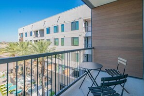 Un balcon avec une table et des chaises, donnant sur une piscine et un immeuble doté de nombreuses fenêtres.