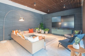 Un salon moderne avec un canapé d’angle, une table basse, un téléviseur fixé au mur et une plante en pot.