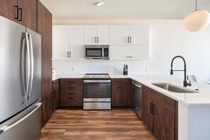 A modern kitchen with stainless steel appliances, white cabinetry, and a wooden floor.
