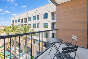 A balcony with a table and chairs, overlooking a swimming pool and palm trees.
