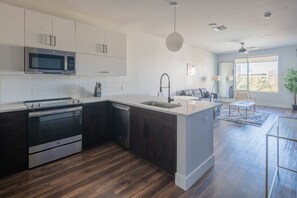 Una cocina moderna con horno empotrado, microondas y lavaplatos, un comedor con mesa y sillas, y un amplio ventanal que proporciona luz natural.